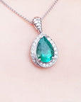 Emerald green teardrop pendant with diamonds on a skin background