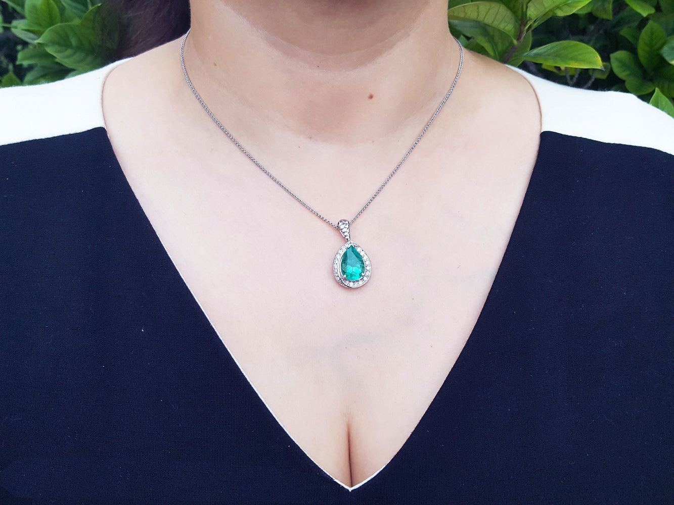 A woman wearing a black top with a natural teardrop emerald pendant necklace.