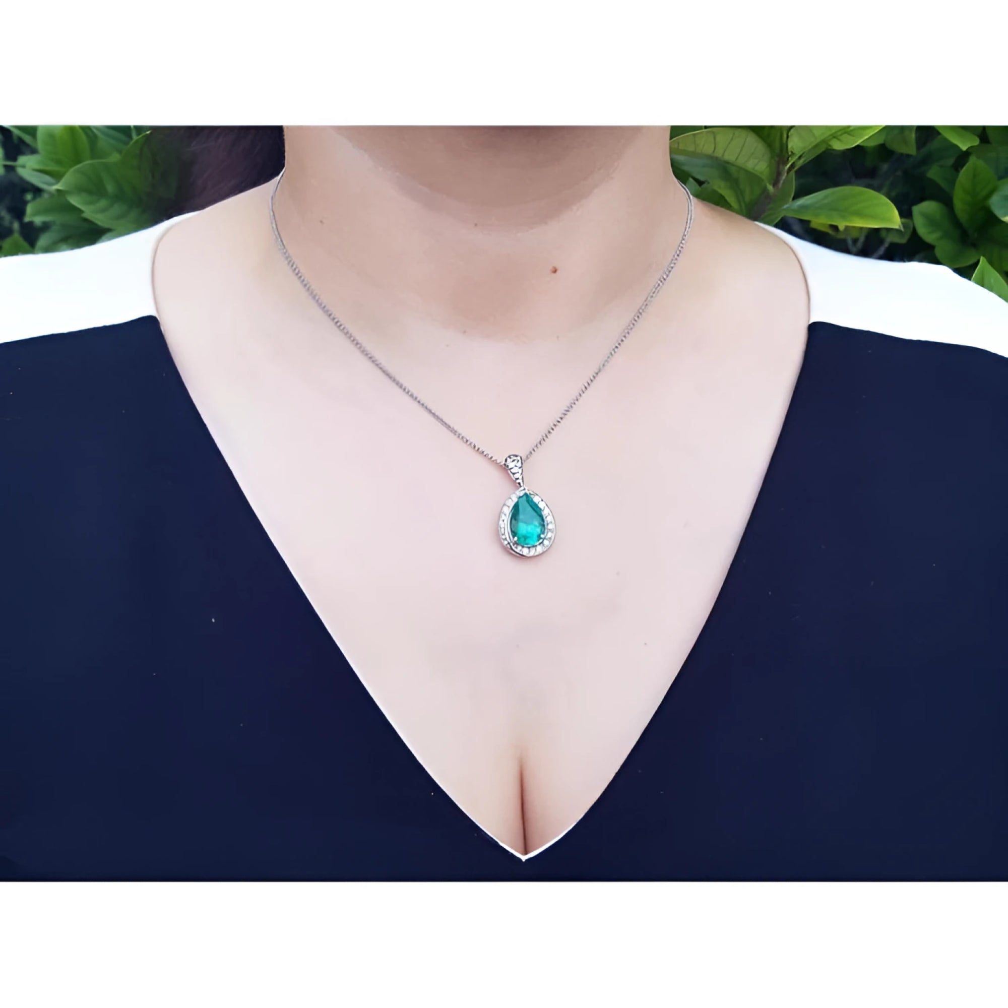 Pear-shaped natural emerald pendant with diamond halo on a 14K white gold chain, worn on a woman's neck.