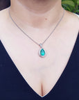 A woman wearing a black top with a natural teardrop emerald pendant necklace.