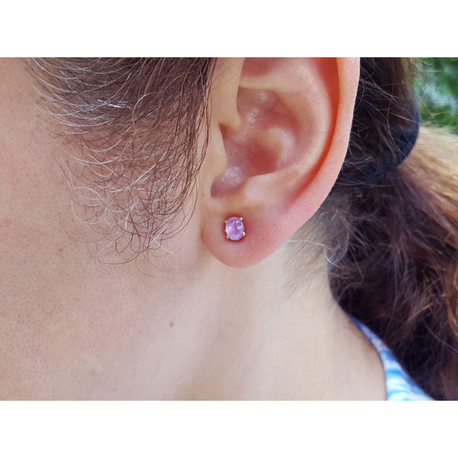Close-up of an ear wearing a pink cabochon sapphire earring with blurred background.