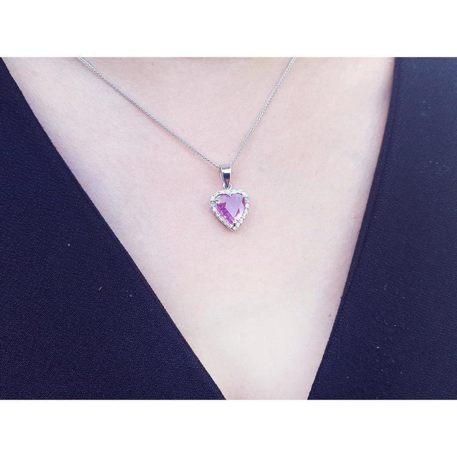 Pink sapphire heart pendant with diamond halo on an 18K white gold chain, worn on a person.