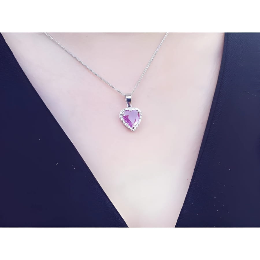 Pink sapphire heart pendant with diamond halo on an 18K white gold chain, worn on a person.
