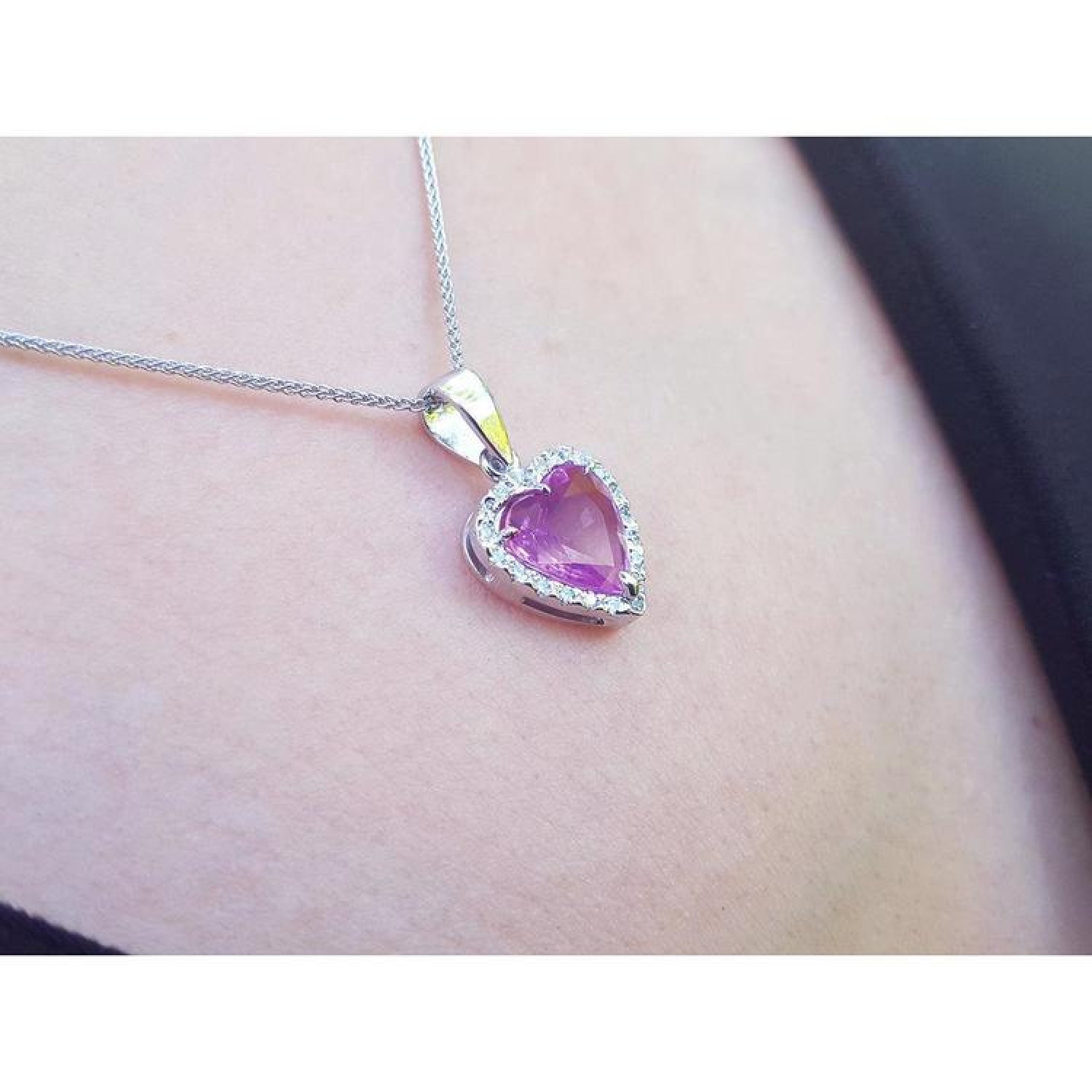Heart-cut pink sapphire pendant with a diamond halo on an 18K white gold chain, worn on a person's neck.