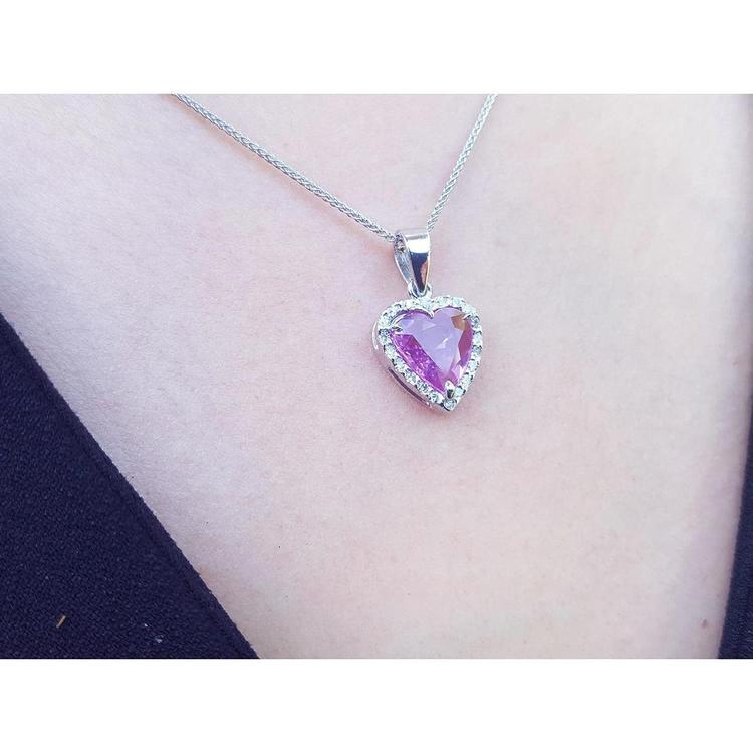 Heart-cut pink sapphire pendant with diamond halo on an 18K white gold chain, worn on a person.