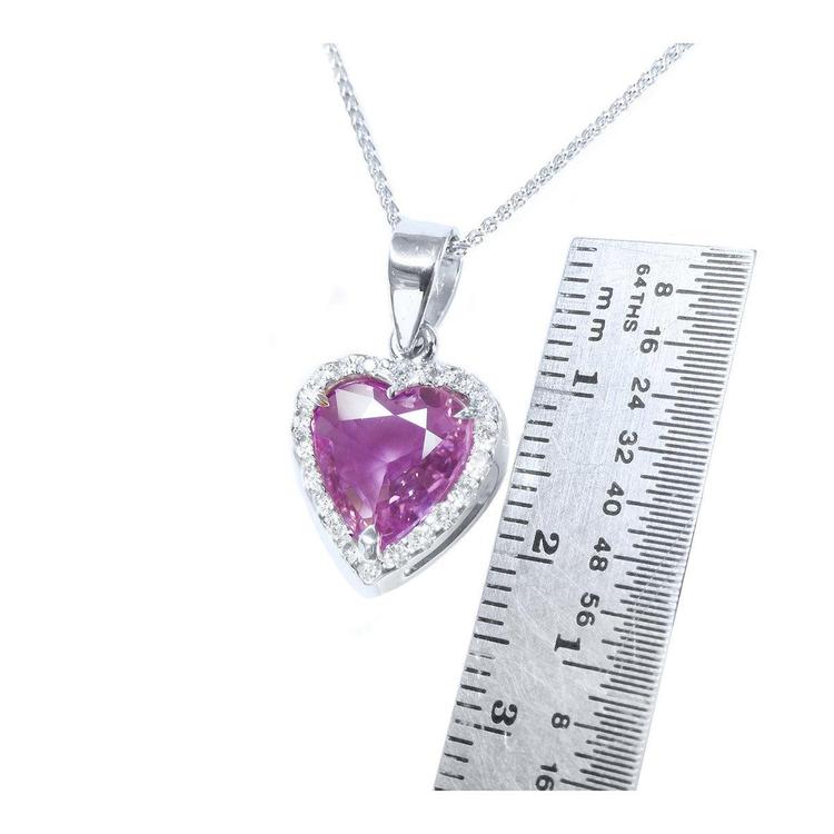 Heart-cut natural pink sapphire pendant with diamond halo on an 18K white gold chain, next to a ruler.