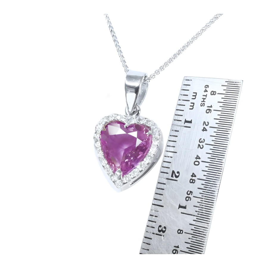 Heart-cut natural pink sapphire pendant with diamond halo on an 18K white gold chain, next to a ruler.
