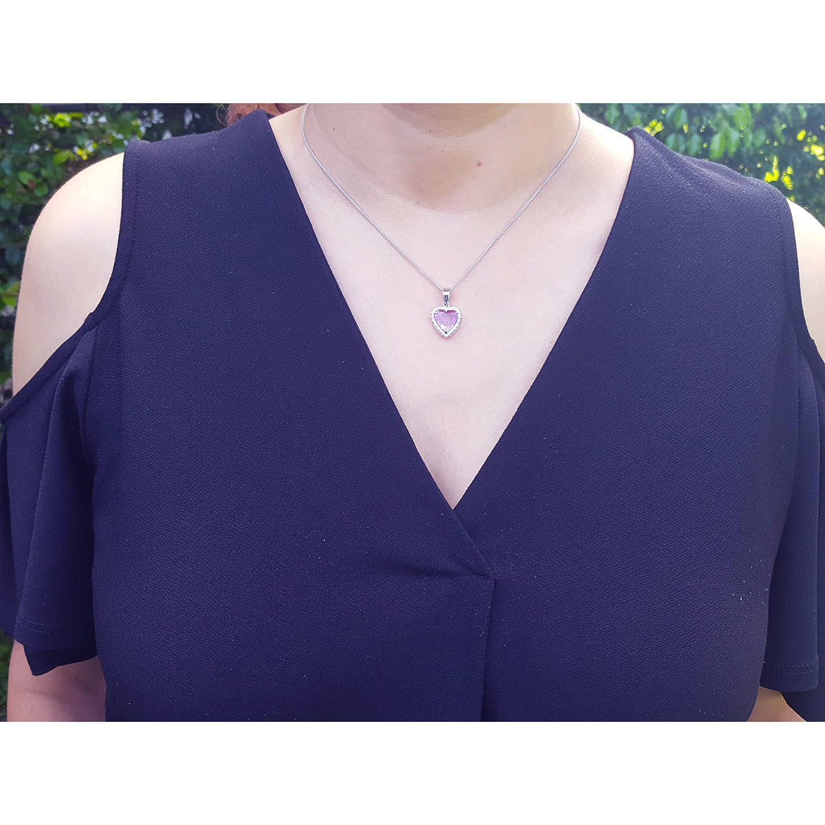 Lady wearing a deep V-neck blue top with a necklace featuring a heart-shaped sapphire pendant.