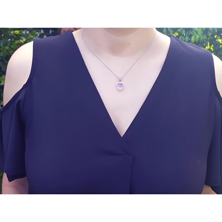 Pink sapphire heart pendant with halo diamonds on an 18K white gold chain, worn on a woman's neck.