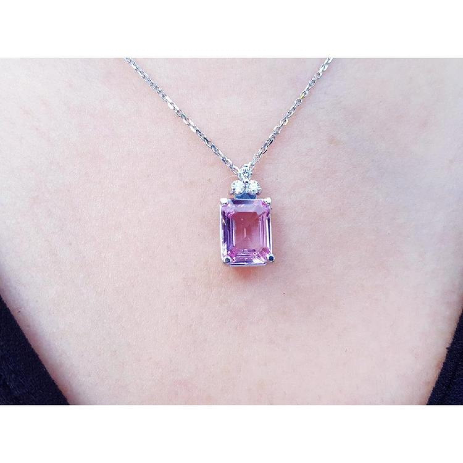 Emerald cut natural pink sapphire necklace in 14K white gold, worn on a person.