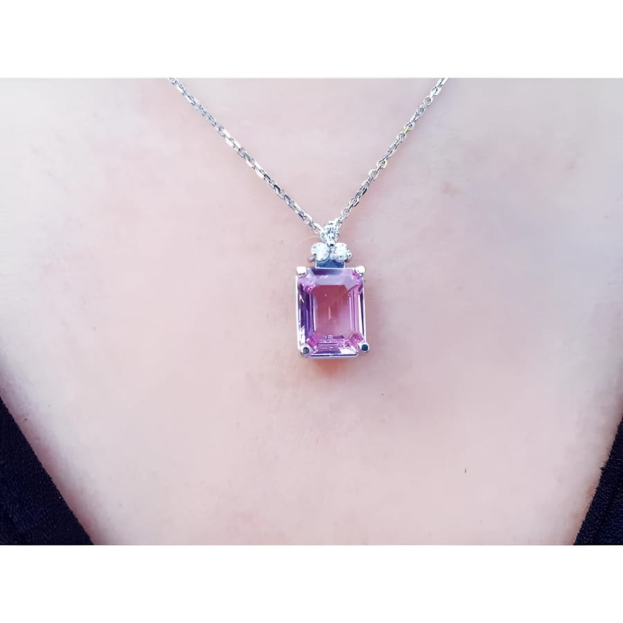 Emerald cut natural pink sapphire necklace in 14K white gold, worn on a person.