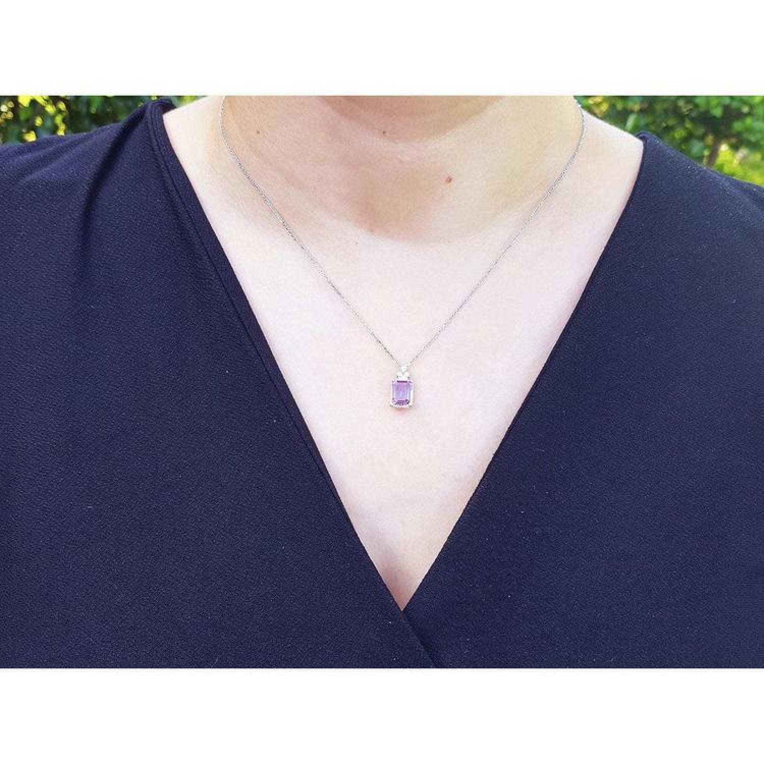 Emerald cut natural pink sapphire necklace in 14K white gold, worn on a person.