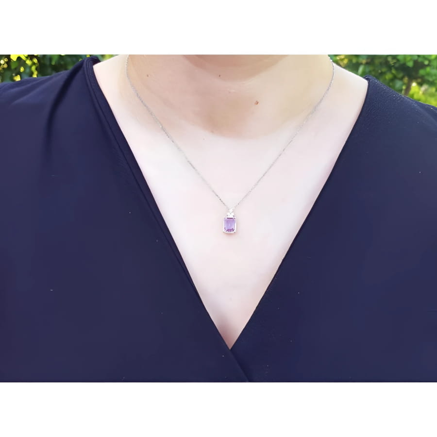 Emerald cut natural pink sapphire necklace in 14K white gold, worn on a person.
