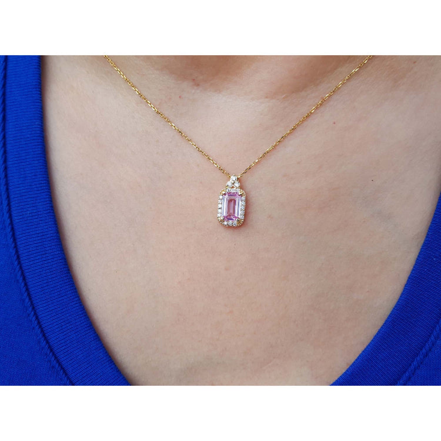 Gold necklace with a natural pink sapphire pendant worn by a person in a blue top.