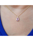 Gold necklace with a natural pink sapphire pendant worn by a person in a blue top.