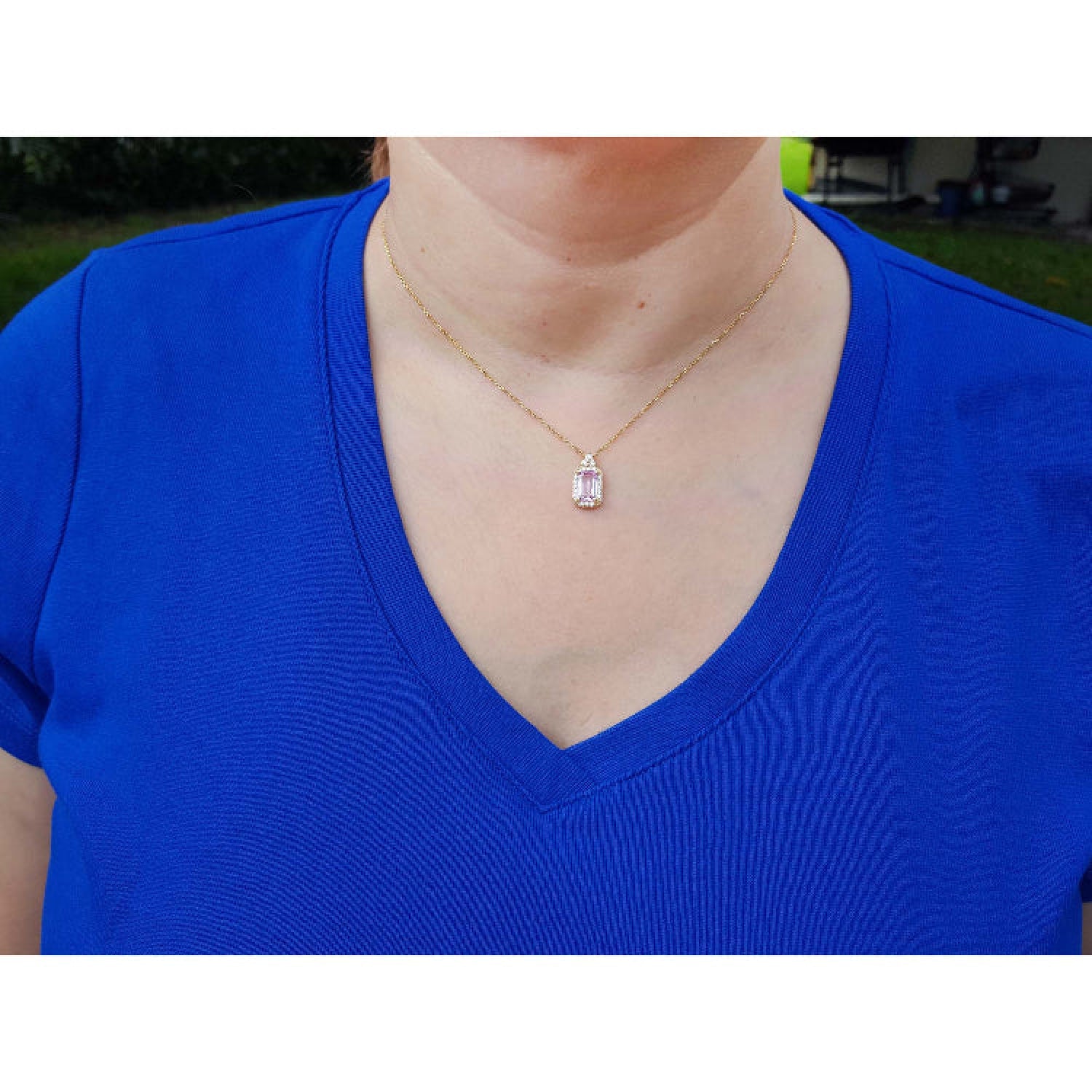 Person wearing a blue shirt with a gold necklace featuring a pink sapphire pendant.