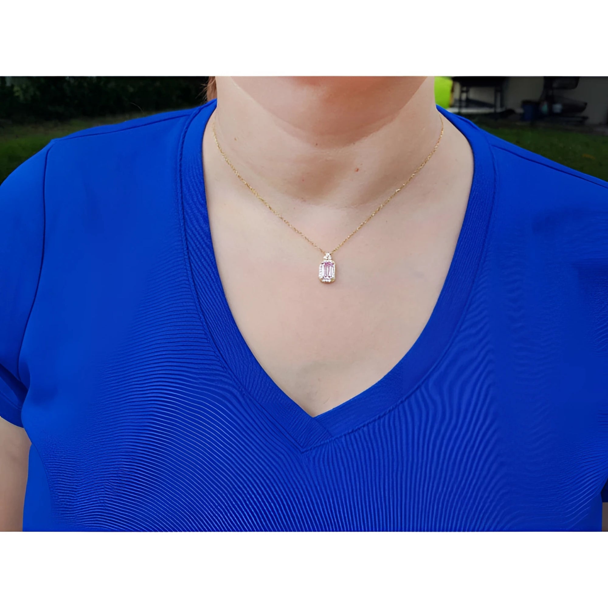 Person wearing a blue shirt with a gold necklace featuring a pink sapphire pendant.