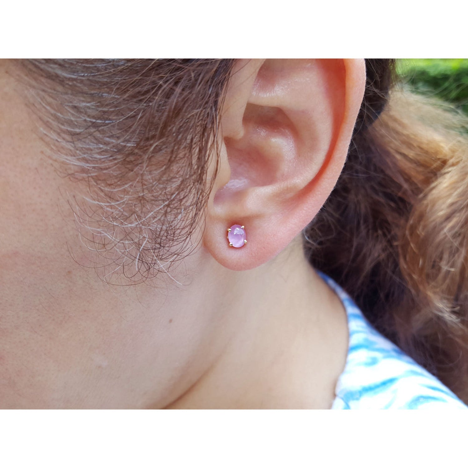 Close-up of a woman wearing a pink sapphire stud earring with blurred background.