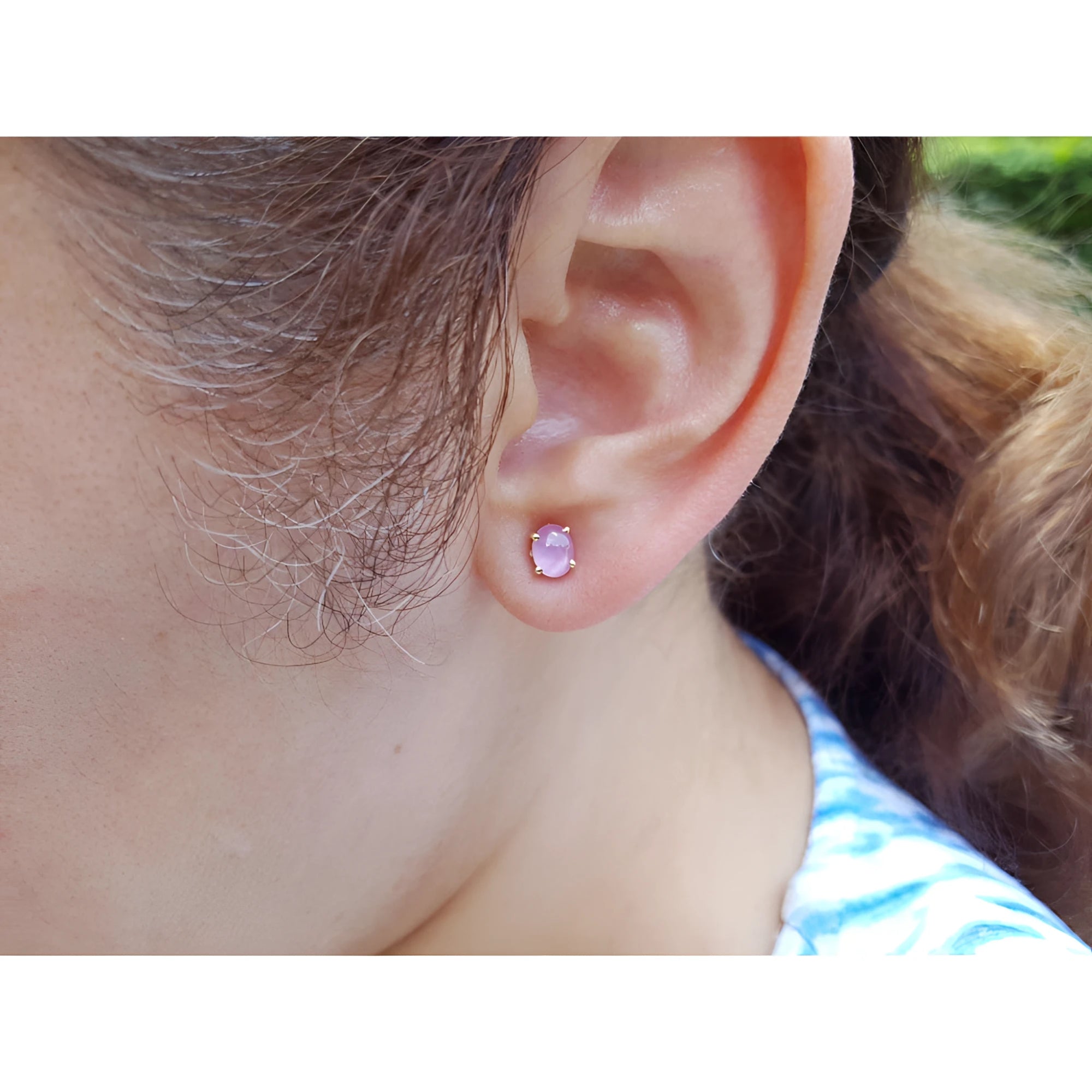 Close-up of a woman wearing a pink sapphire stud earring with blurred background.