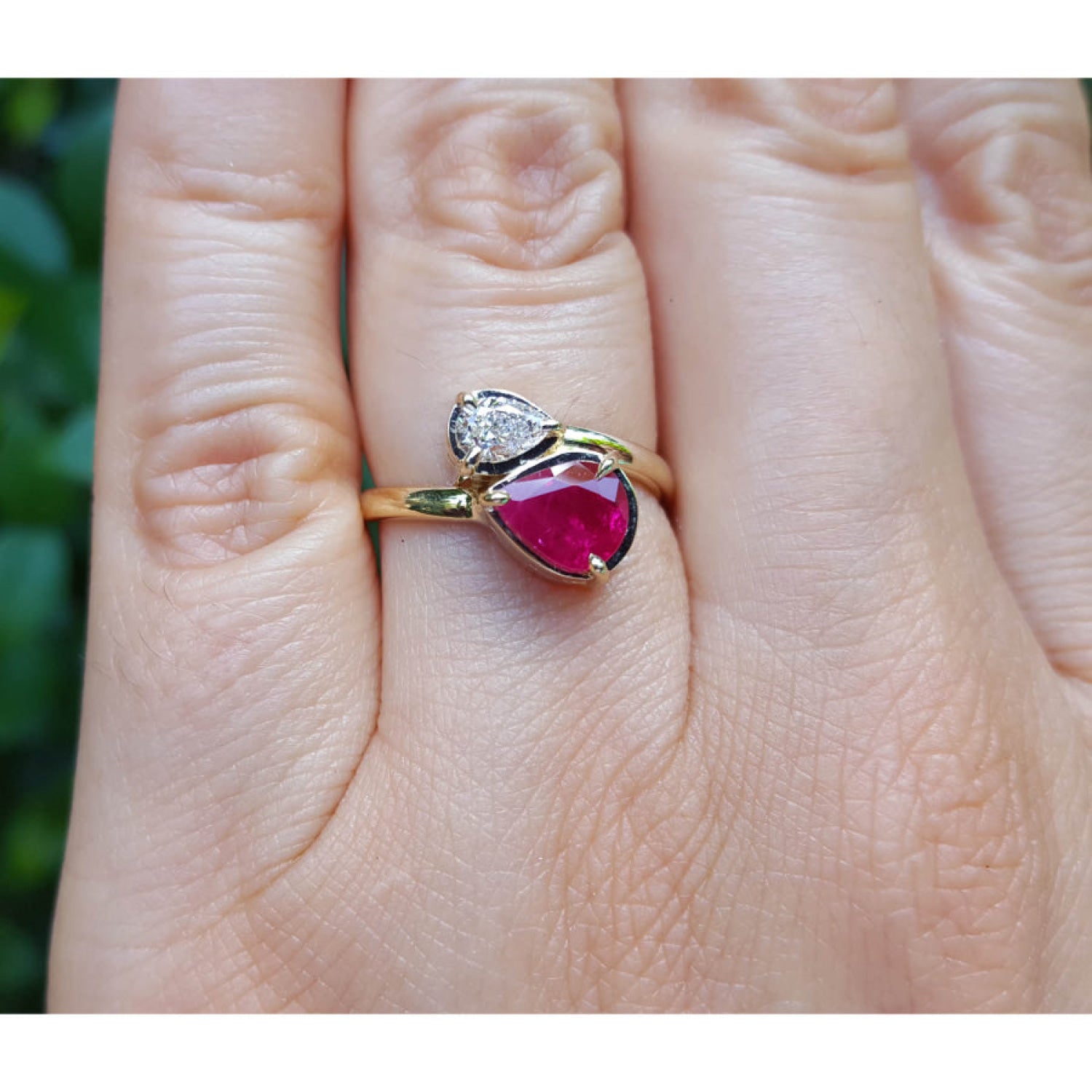 A natural ruby and diamond you and me ring made of 18k yellow gold, shown worn on a person's finger.