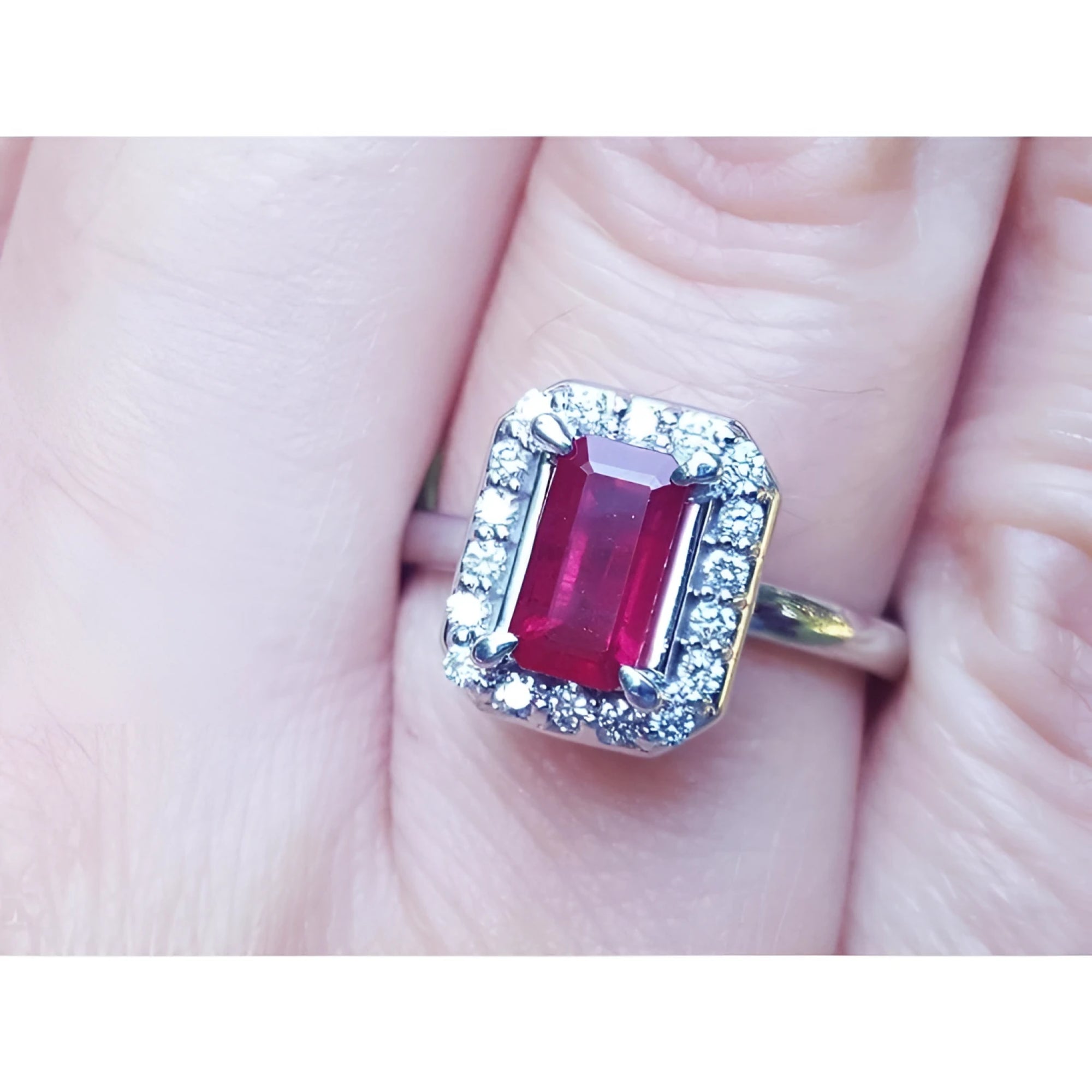 Emerald-cut ruby ring with diamond halo, set in 14K white gold on a finger.