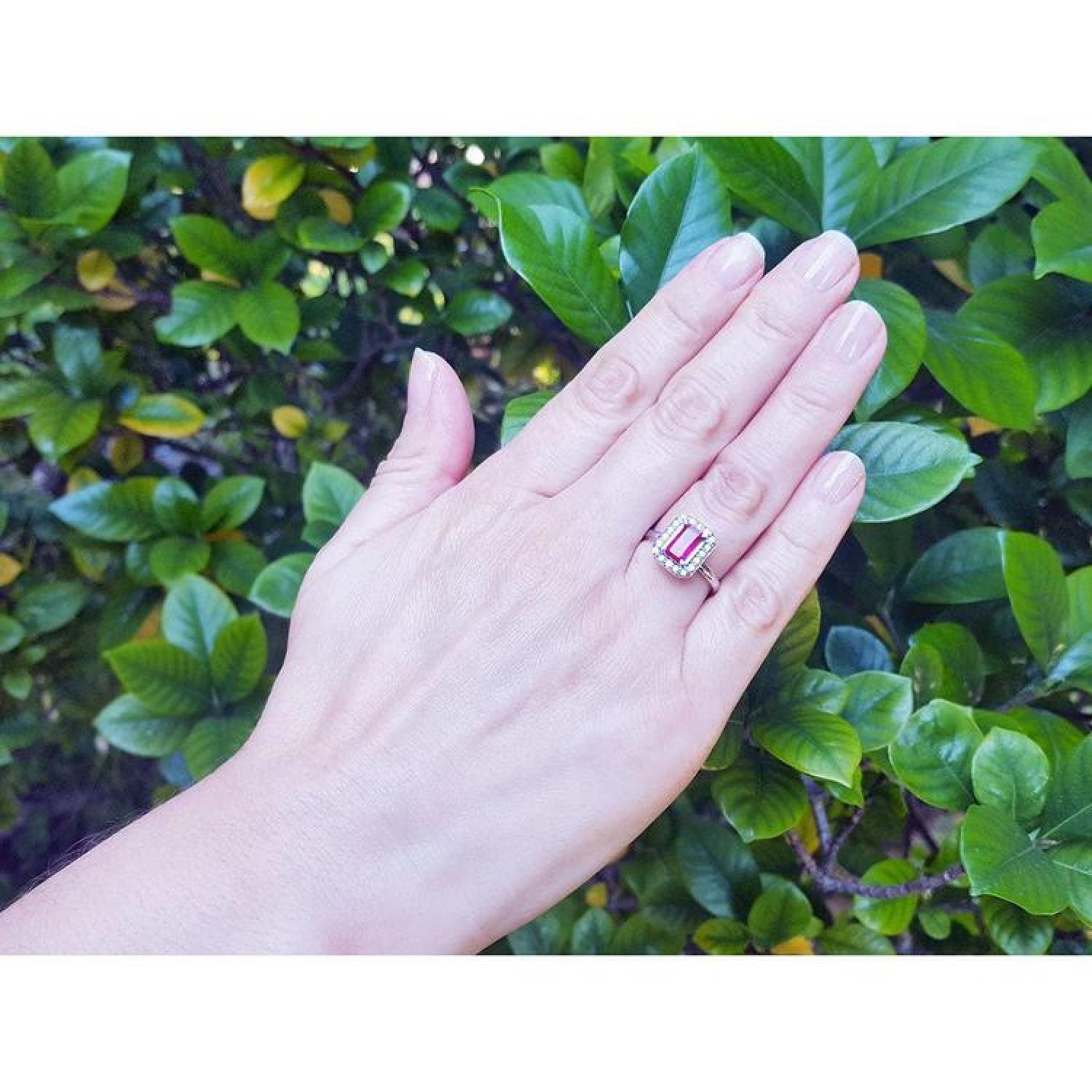 Women's 14K white gold ring with an emerald-cut deep red ruby and diamond halo on a hand.