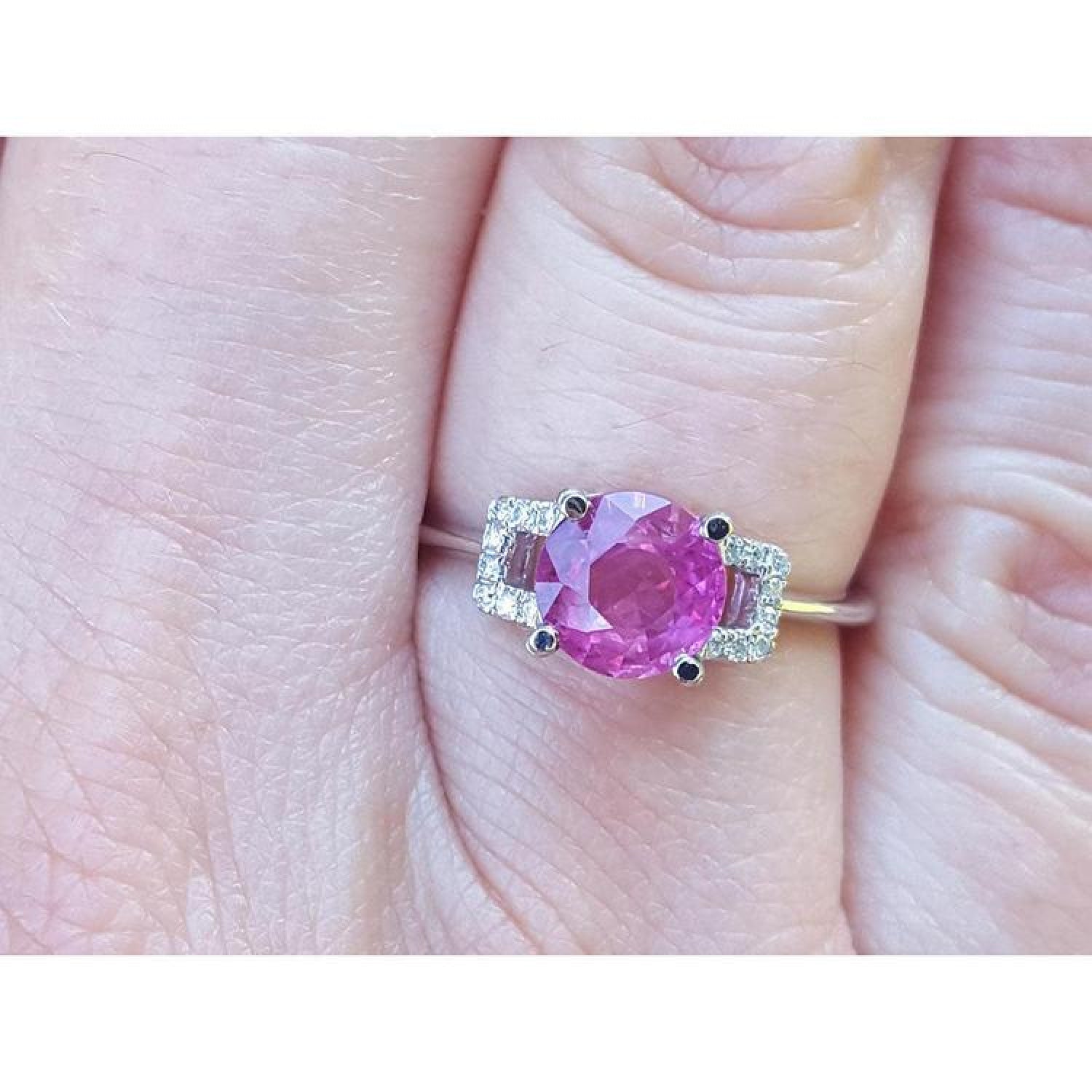 Round cut pinkish-red Mozambique ruby ring with accented diamonds in 14k white gold on a finger.