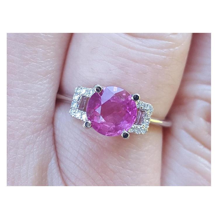 Ring with a pink ruby gemstone round cut and diamond accents on a finger