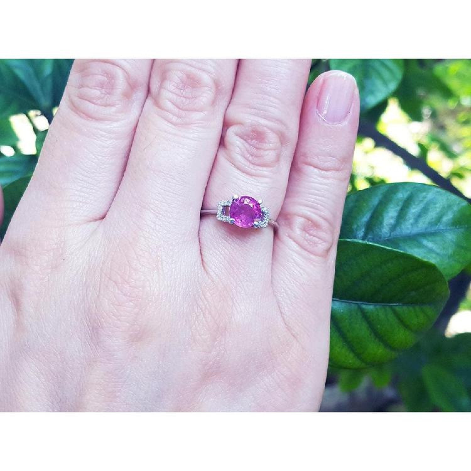Round cut pinkish-red Mozambique ruby ring with accented diamonds in 14k white gold on a hand.