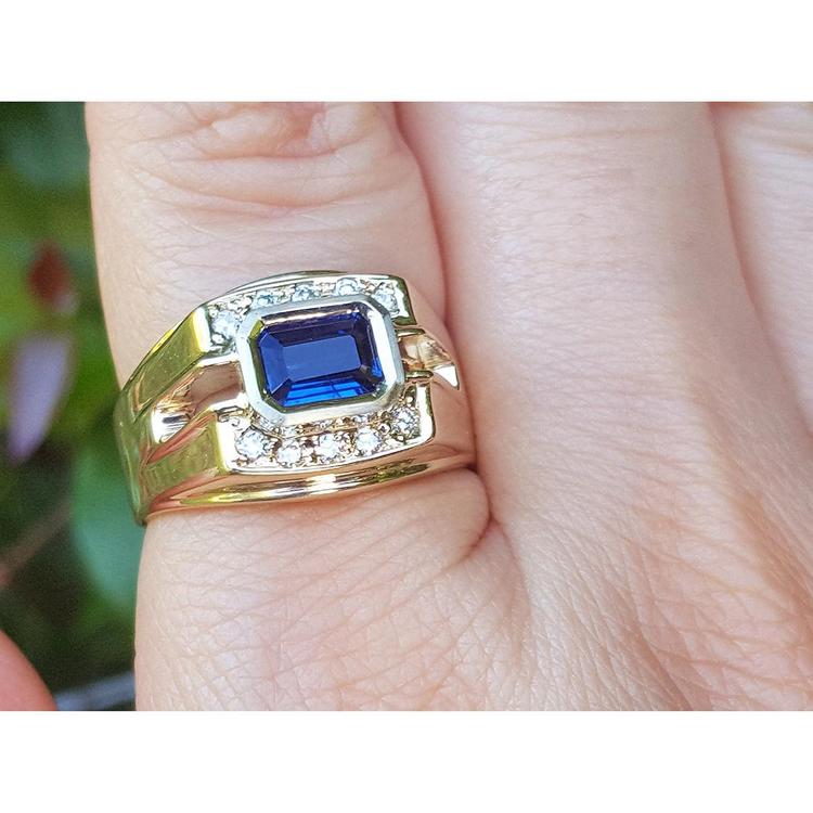 Gold ring with a blue natural sapphire and diamonds on a finger against a blurred background