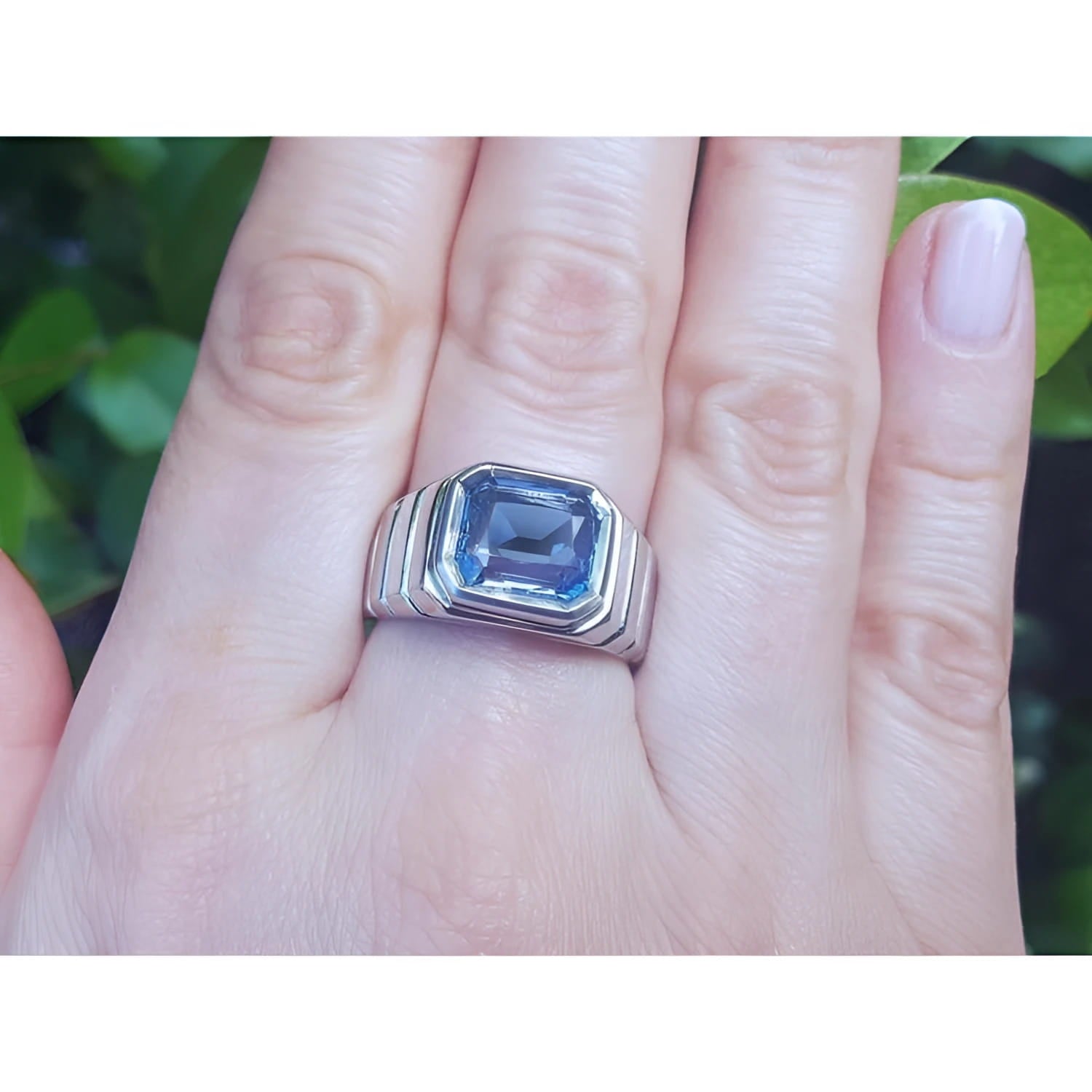 Men's 18K white gold ring with a bezel-set, emerald-cut vivid blue sapphire on a hand.