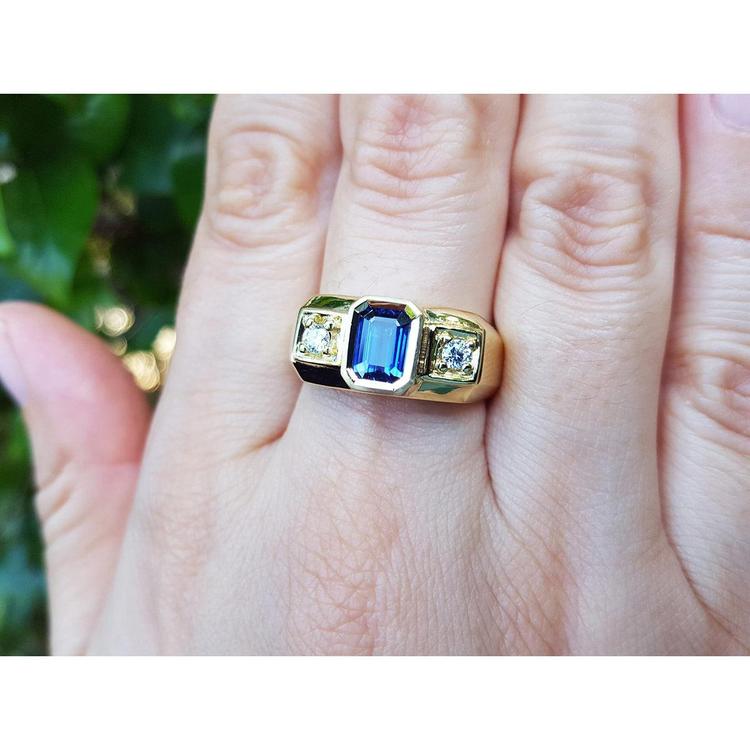 Gold ring with a blue natural sapphire gemstone on a hand against a blurred green background