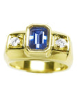 Men’s natural sapphire ring featuring an emerald-cut vibrant medium blue stone in a bezel setting, accented by side round-cut diamonds, crafted in 14K yellow gold.