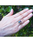 A woman's hand wearing a fine watermelon tourmaline ring against a leafy background.
