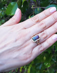 A woman's hand wearing a fine watermelon tourmaline ring against a leafy background.