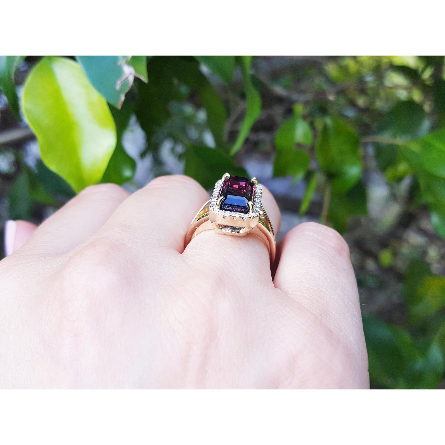 Ring with gemstones tourmaline on a hand against a green leafy background.