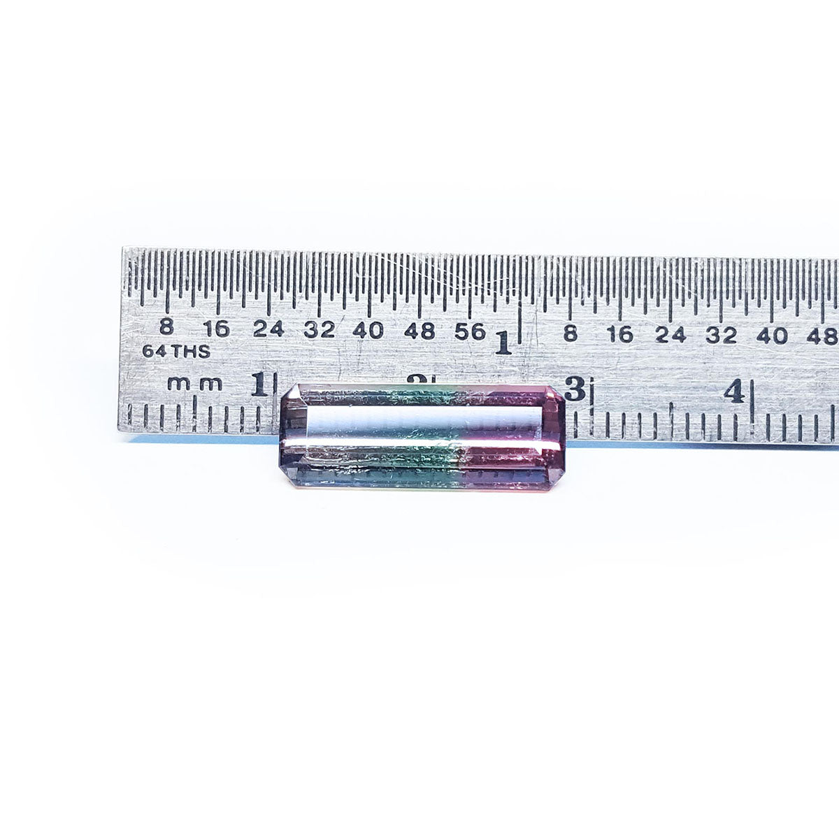 A rectangular natural watermelon tourmaline next to a ruler on a white background.