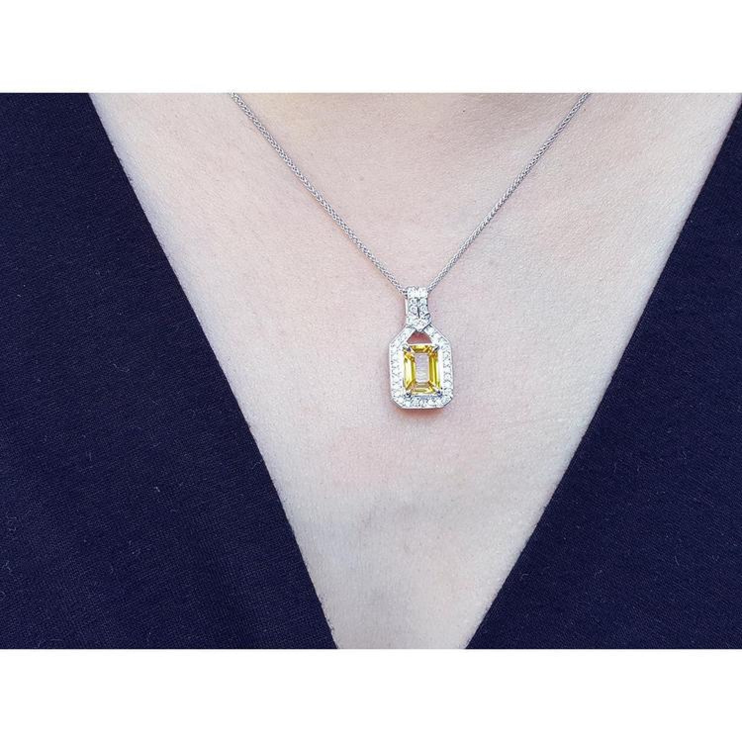 Emerald cut yellow sapphire halo diamond pendant on an 18K white gold chain, worn on a woman.