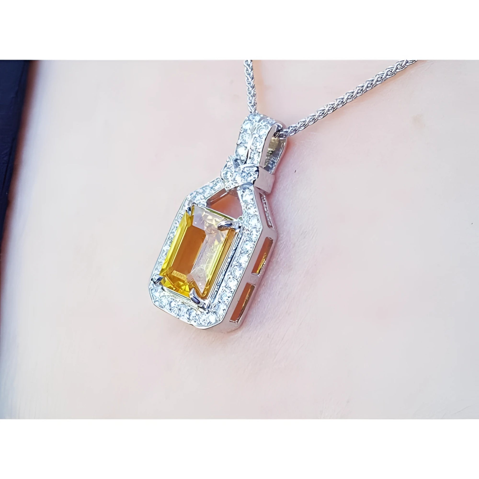Emerald cut yellow sapphire pendant with halo diamonds on an 18K white gold chain, worn on a woman's neck.