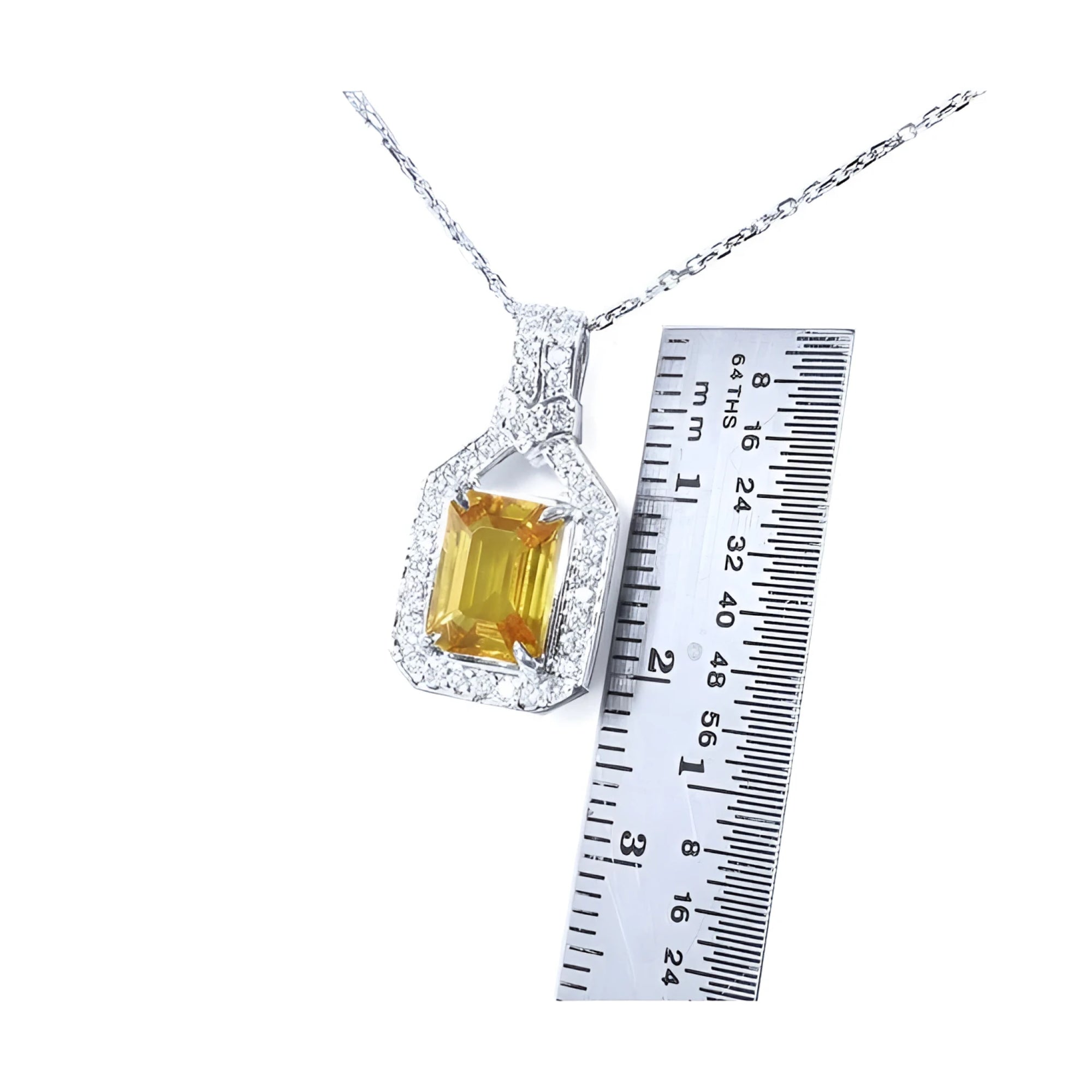 Emerald cut yellow sapphire pendant with diamond halo on an 18K white gold chain, shown with a ruler.