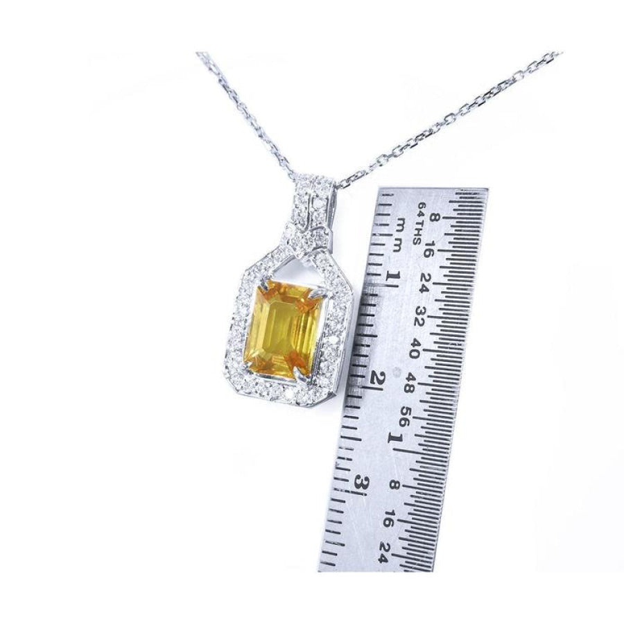 Emerald cut yellow sapphire pendant with diamond halo on an 18K white gold chain, shown with a ruler.