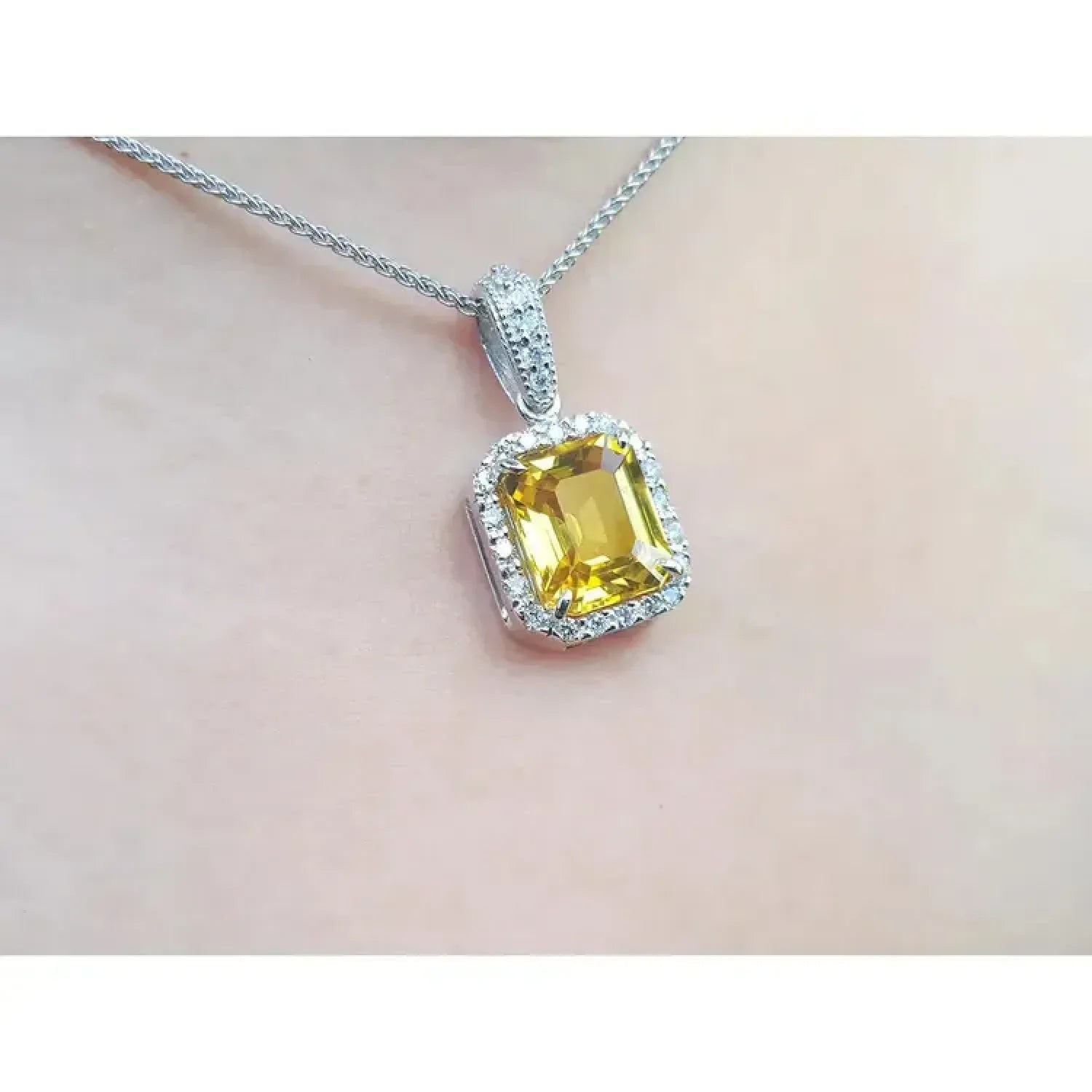 Emerald cut yellow sapphire pendant with diamond halo on an 18K white gold chain.