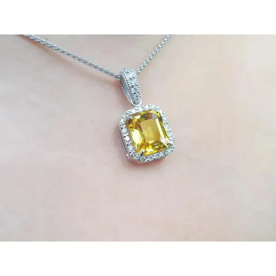 Emerald cut yellow sapphire pendant with diamond halo on an 18K white gold chain.