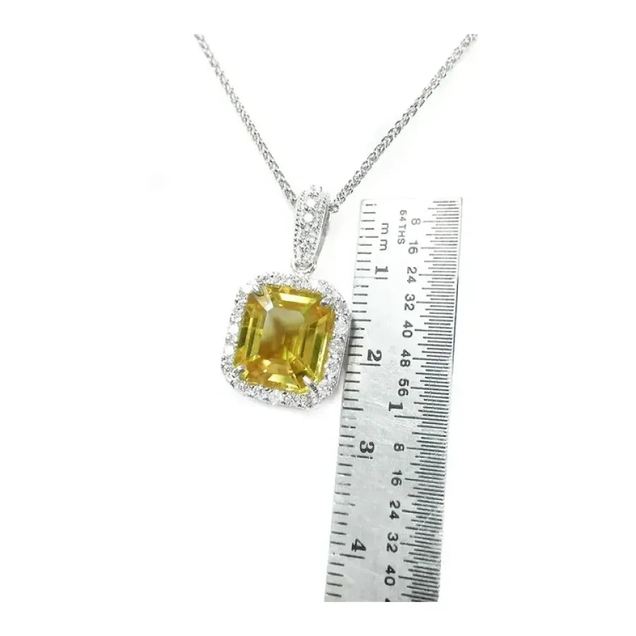 6.01 ct. emerald cut yellow sapphire pendant with diamond halo in 18K white gold, next to a ruler.