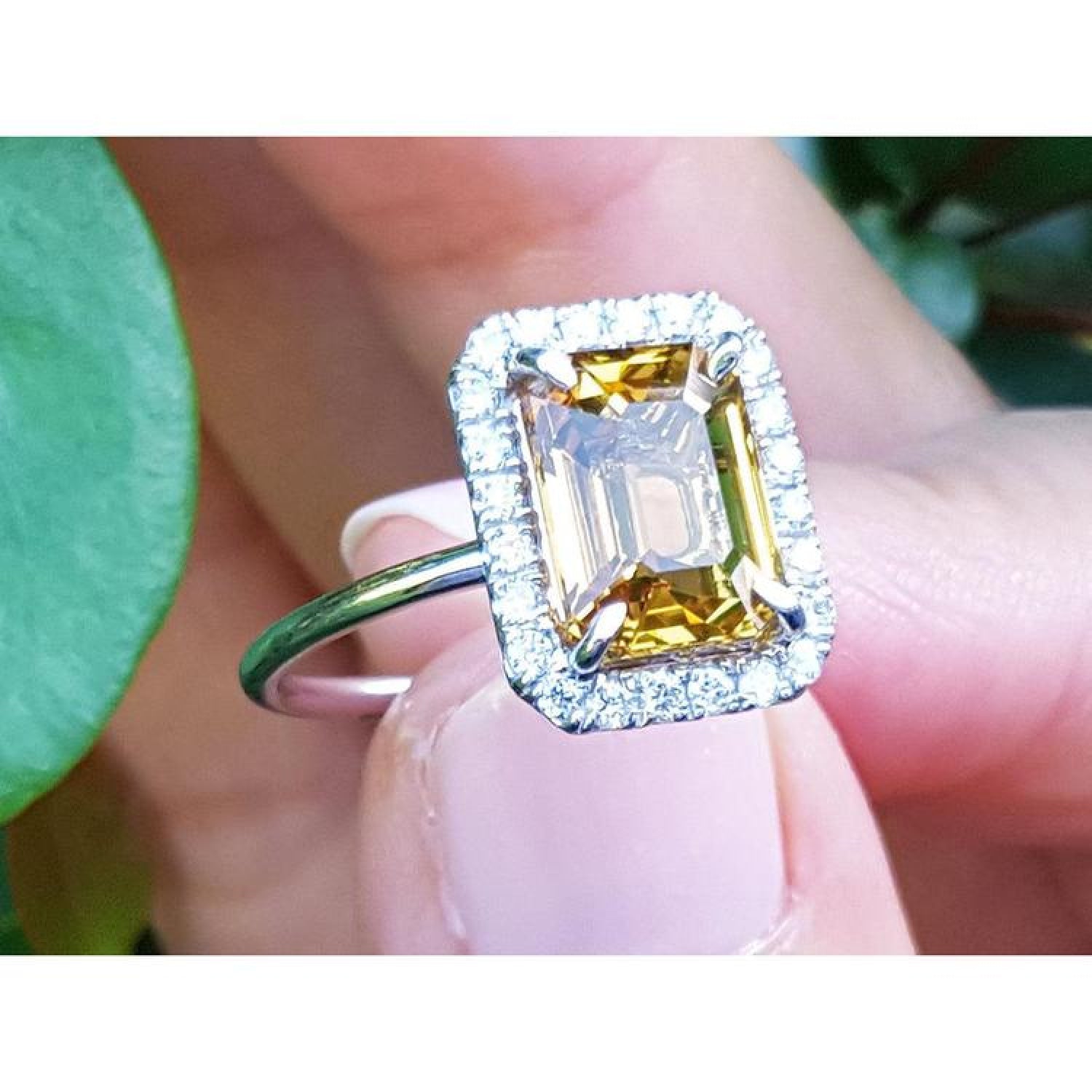 Emerald cut 4.59 ct yellow sapphire halo diamond ring in 14K white gold, worn on a finger.