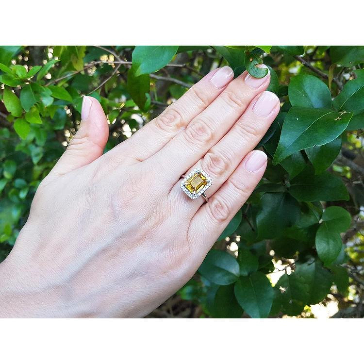 Emerald cut 4.59 ct yellow sapphire ring with diamond halo in 14K white gold on a hand.