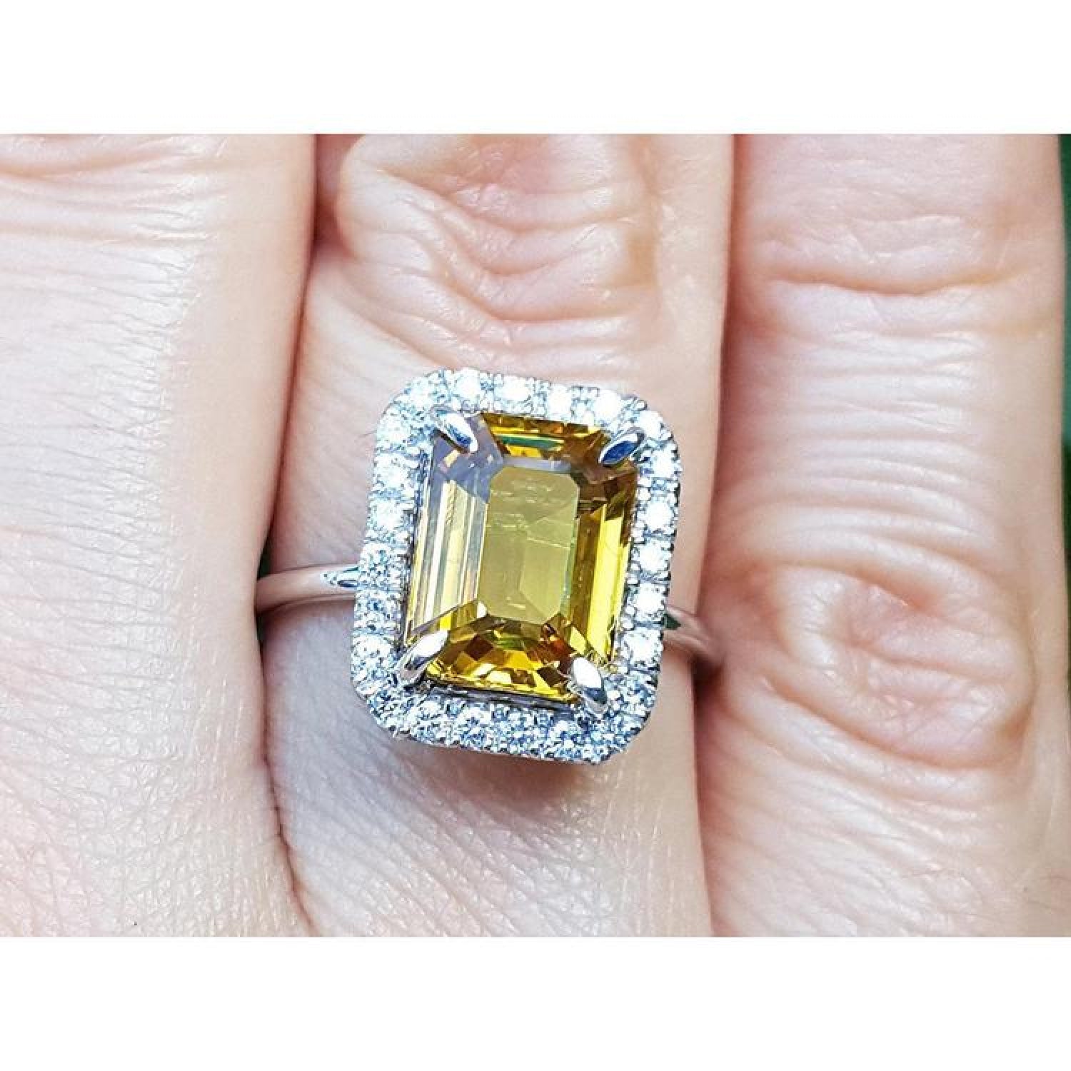 Emerald cut yellow sapphire ring with diamond halo in 14K white gold on a finger.