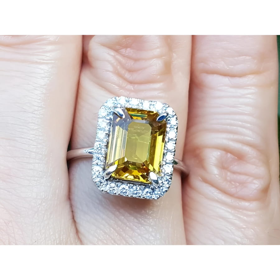 Emerald cut yellow sapphire ring with diamond halo in 14K white gold on a finger.