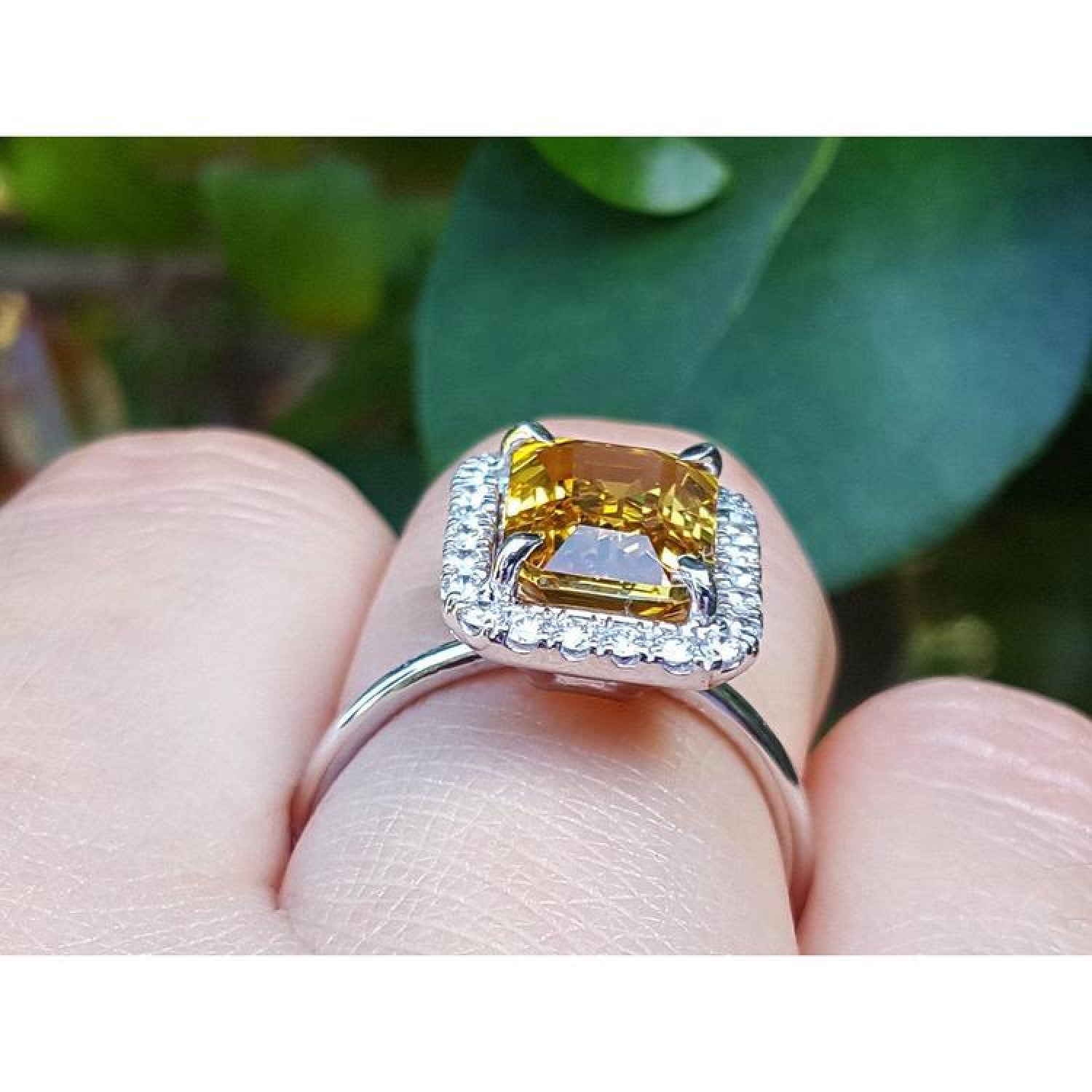 Emerald cut yellow sapphire ring with diamond halo in 14K white gold on a finger.