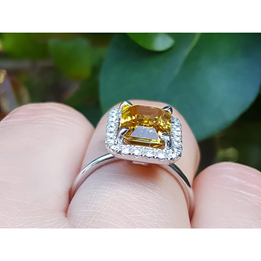 Emerald cut yellow sapphire ring with diamond halo in 14K white gold on a finger.
